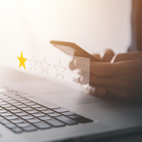 a person in front of their laptop, typing on their phone. Overlay of a 5-star review system
