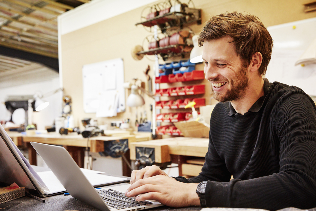 male business owner smiling at a laptop in a workshop