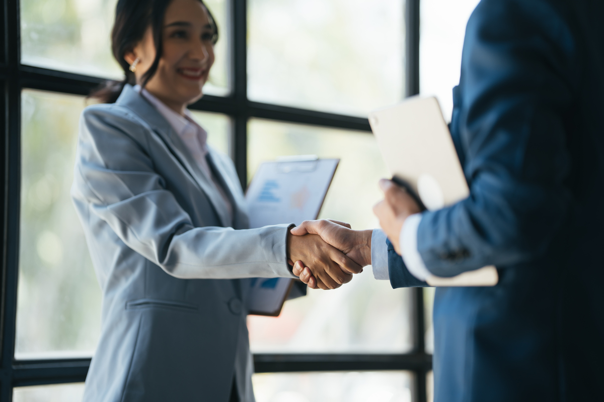 two business professionals holding clipboards and shaking hands