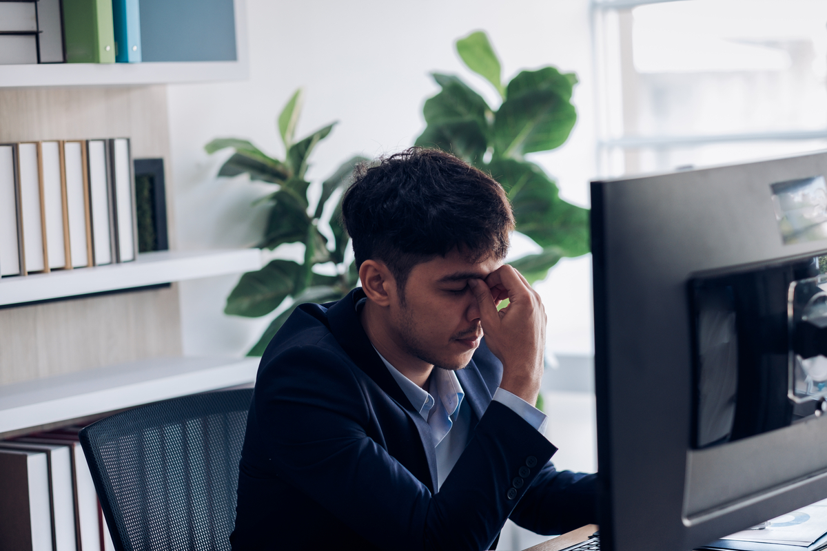 a man sitting at a computer pinching the bridge of his nose
