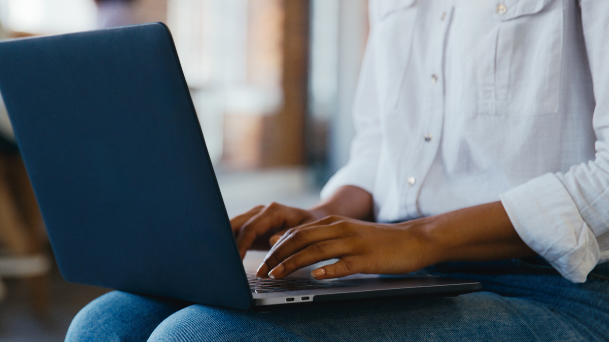 closeup of someone sitting with a laptop in their lap, typing