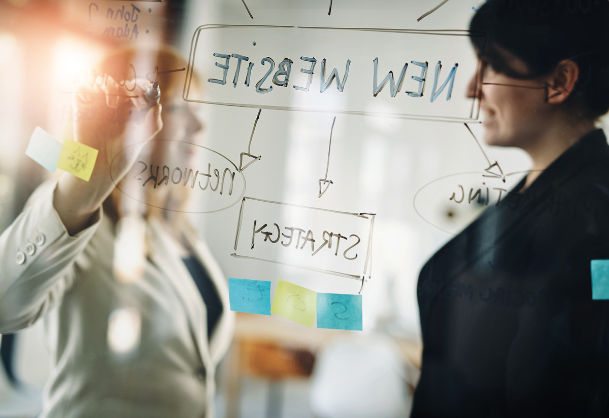 two women writing on a white board about website strategy