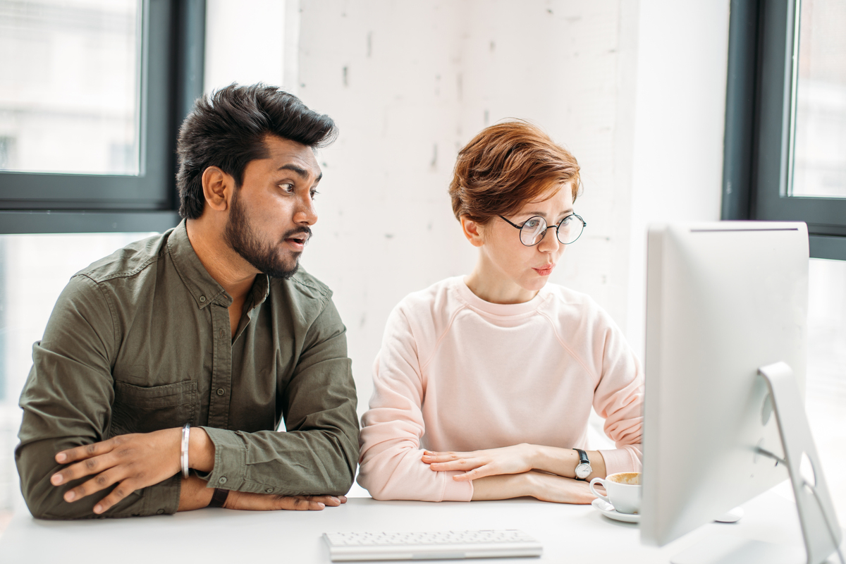 Two coworkers reviewing information together on a desktop computer in an office.