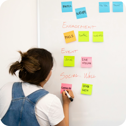 a woman standing and presenting with sticky notes on the wall behind her and laptop sitting on a desk