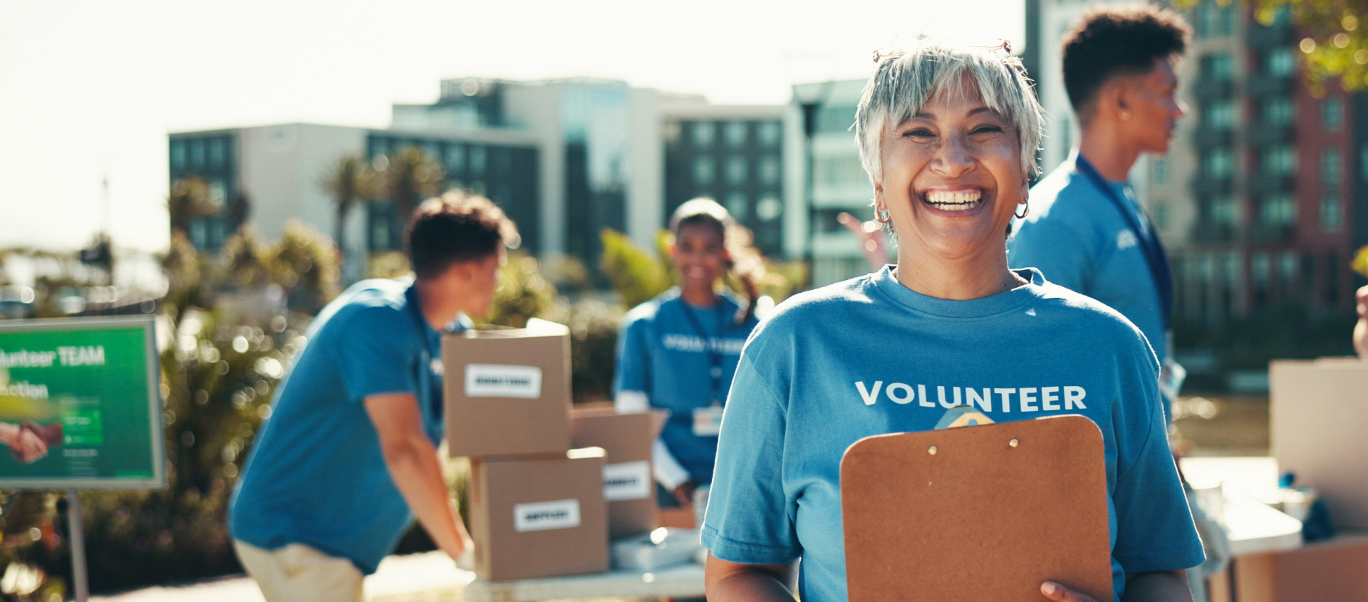 Volunteer woman smiling holding clipboard while others are organizing boxes
